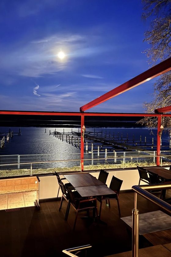 Die Terrasse bei Nacht, der Mond steht über dem Bootshafen